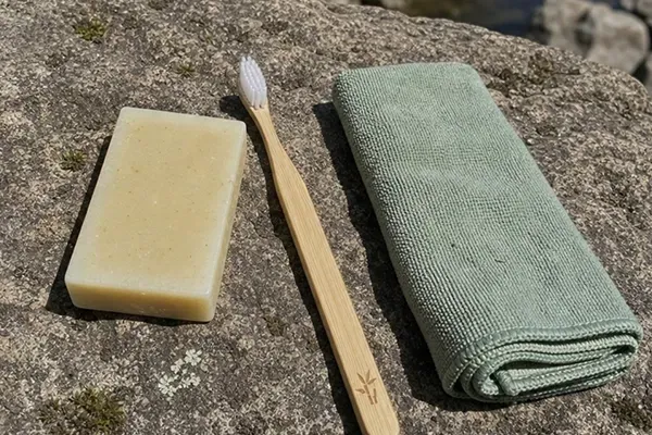 matériel d'hygiène de randonnée étalé sur une roche, savon solide, brosse à dents en bambou, petite serviette microfibre